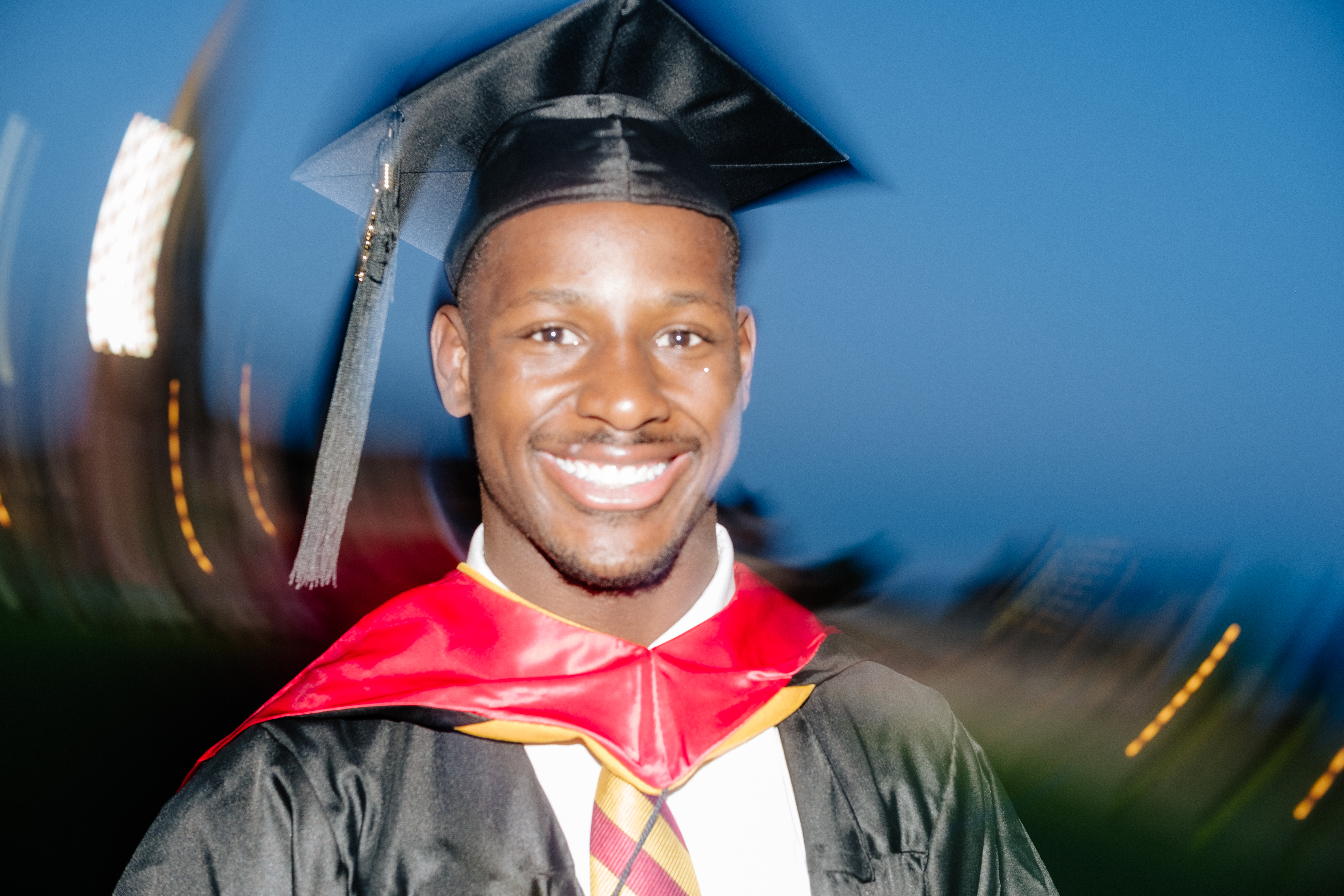 Graduate beaming in cap and gown with dreamy bokeh lights at night